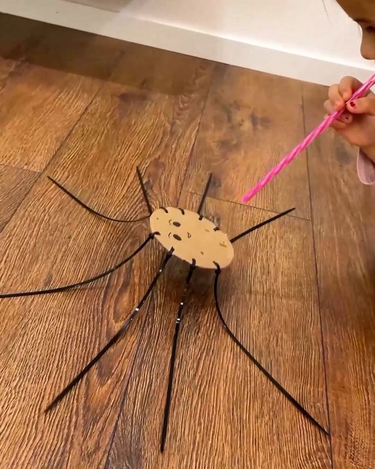 A child playing with a cardboard spider on the floor