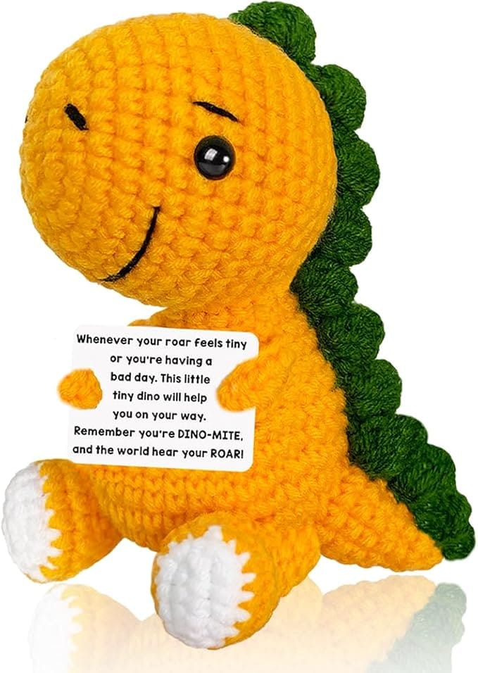 a crocheted dinosaur toy holding a sign that says "Whenever your roar feels tiny or you're having a bad day, this little tiny dino will help you on your way. Remember you're DINO-MITE, and let the world hear your ROAR!"
